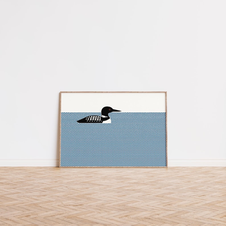 May include: Framed art print featuring a stylized illustration of a loon swimming in blue water. The loon is black and white with a long beak. The water has a textured pattern, and the sky is white.