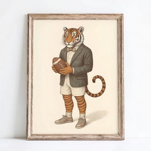 May include: A framed print depicting a tiger in a suit, shorts, and trainers, holding a rugby ball. The tiger has orange and black stripes, a bow tie, and a striped tail. The artwork has a vintage, whimsical style, with a cream-colored background.