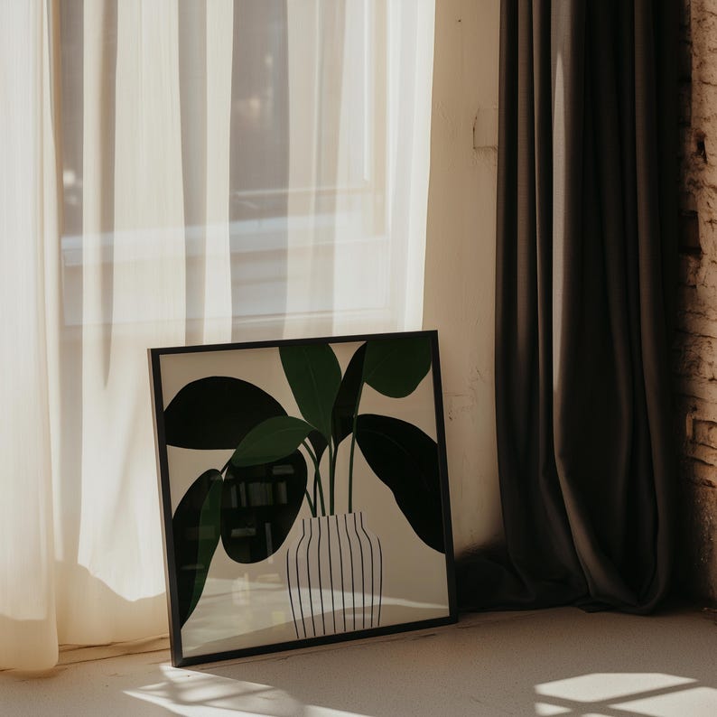 May include: A framed art print featuring a stylized illustration of a potted plant with large green leaves. The plant is in a white vase with vertical black stripes. The frame is black, and the artwork is leaning against a wall near a window.