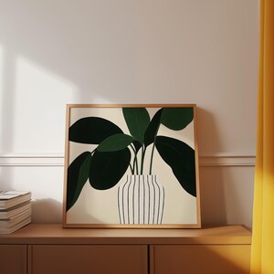 May include: A framed art print featuring a stylized illustration of a potted plant. The plant has large, dark green leaves and is in a white vase with vertical black stripes. The frame is a light brown color, and the background is a neutral beige.