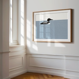 May include: A framed art print featuring a minimalist illustration of a loon swimming in blue water. The loon is black and white, and the water has a textured pattern. The frame is a light wood color.