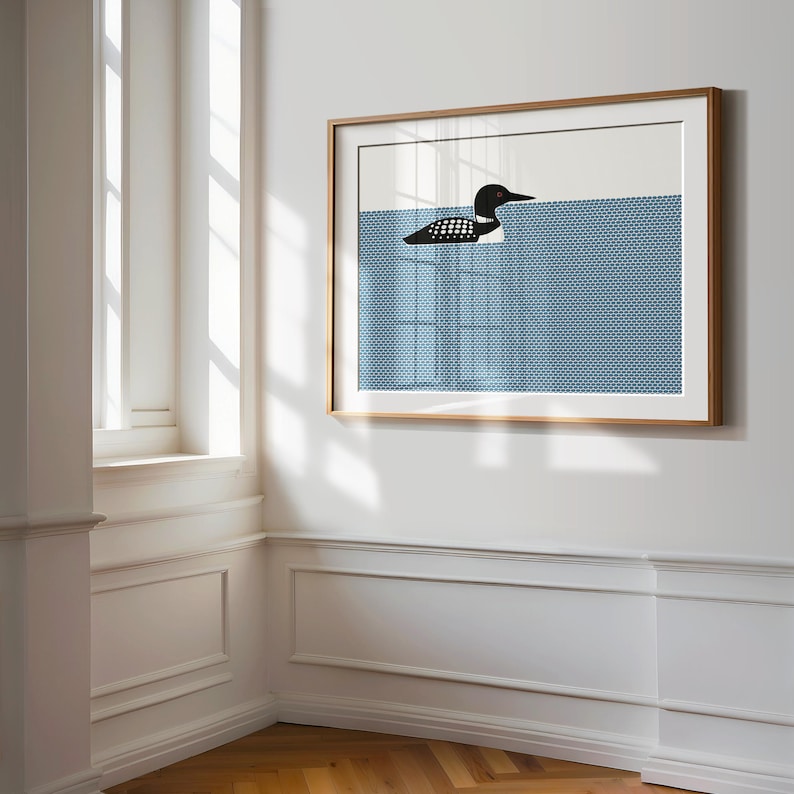 May include: A framed art print featuring a minimalist illustration of a loon swimming in blue water. The loon is black and white, and the water has a textured pattern. The frame is a light wood color.