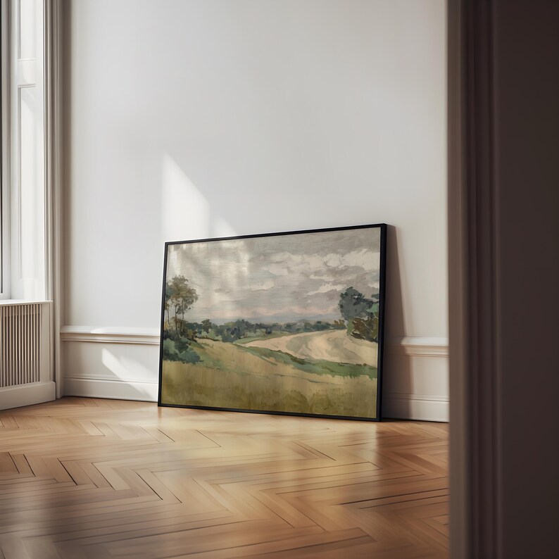 K&ouml;nnte beinhalten: Ein gerahmtes Landschaftsgem&auml;lde mit schwarzem Rahmen. Das Kunstwerk zeigt ein Feld mit einem gewundenen Pfad, B&auml;umen und einem bew&ouml;lkten Himmel. Die Farbpalette umfasst Gr&uuml;n-, Gelb- und Graut&ouml;ne und erzeugt eine ruhige und nat&uuml;rliche Szene.