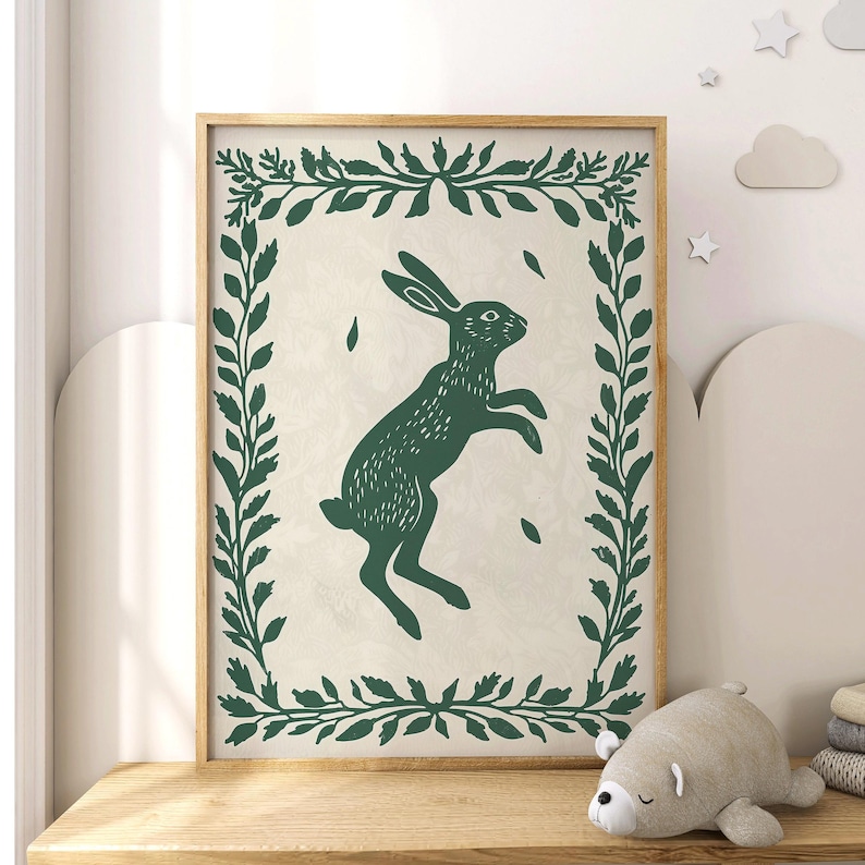 May include: A green and white print of a rabbit jumping in a leafy frame. The rabbit is silhouetted in dark green against a cream background.