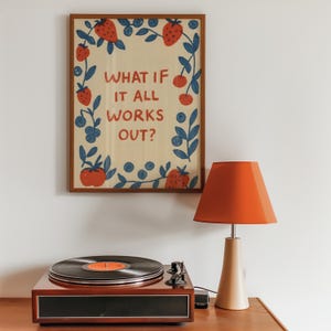 K&ouml;nnte beinhalten: Ein gerahmter Druck mit dem Text "WHAT IF IT ALL WORKS OUT?" umgeben von einem Rand aus roten Erdbeeren, Blaubeeren und gr&uuml;nen Bl&auml;ttern. Ein Vintage-Plattenspieler und eine orangefarbene Lampe befinden sich darunter.