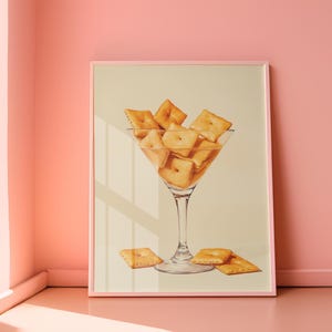 May include: A framed print of a martini glass filled with square-shaped crackers. The glass is on a light beige background.