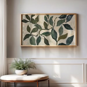 May include: A framed painting of a stylised green leafy branch on a white background. The painting is in a gold frame and is hanging on a white wall.