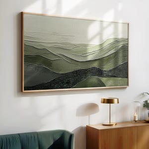 May include: A framed landscape painting with a textured, layered effect. The artwork features rolling hills in shades of green, from light olive to deep forest, creating a sense of depth and dimension. The frame is a light wood tone, complementing the artwork's natural palette.