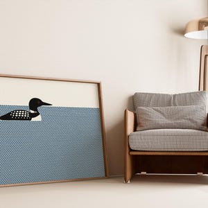May include: A framed art print featuring a black and white loon swimming in blue water. The artwork is displayed next to a wooden armchair with a checkered pattern and a modern floor lamp with a gold shade.
