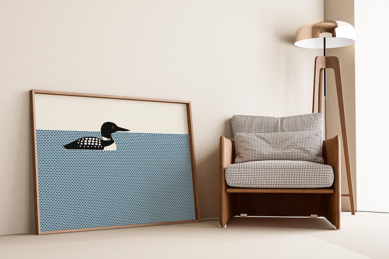 May include: A framed art print featuring a black and white loon swimming in blue water. The artwork is displayed next to a wooden armchair with a checkered pattern and a modern floor lamp with a gold shade.