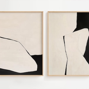 May include: Two abstract paintings in black and white with a beige background. The paintings are framed in natural wood.