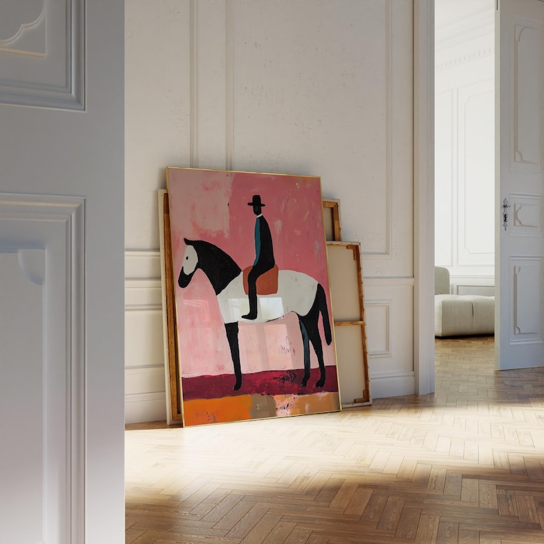 K&ouml;nnte beinhalten: Ein gerahmtes Gem&auml;lde, das ein schwarz-wei&szlig;es Pferd mit einer Person in einem schwarzen Hut und einem blauen Hemd zeigt, die darauf reitet. Der Hintergrund ist ein abstraktes Design in Rosa und Orange.