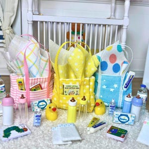 以下が含まれることがあります： ピンクのストライプ、黄色の水玉模様、青い星柄のミニチュア布製トートバッグ3点。それぞれに柄入りの布が詰められています。セットには、小さな哺乳瓶、黄色いゴム製のアヒル、ミニチュアの本、ベビーケア用品の小さな箱が含まれています。