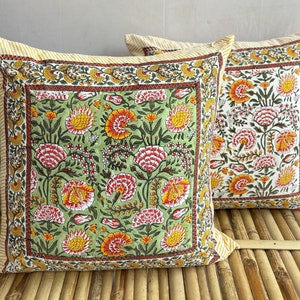 Puede incluir: Dos almohadas cuadradas con un patrón floral. Las almohadas tienen un fondo verde con flores amarillas, rojas y blancas. Las almohadas tienen un borde amarillo y blanco.
