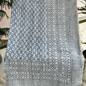 May include: A blue and white cotton quilt with a floral pattern. The quilt is folded and displayed on a wooden chair.