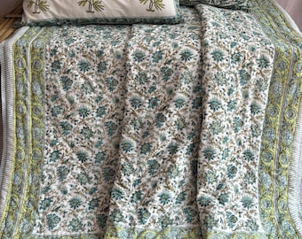 May include: A white cotton quilt with a green floral print and a light green border. The quilt is folded and displayed on a bed with two matching pillowcases.