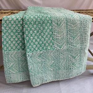 Może przedstawiać: Zielono-biała kołdra kantha z kwiatowym i geometrycznym wzorem. Kołdra jest złożona i wystawiona na drewnianym stole.