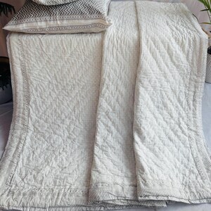 May include: A white quilted bedspread with a geometric pattern and matching pillowcases. The pillowcases and the border of the bedspread feature a grey and white striped design. The bedding is displayed on a white surface.