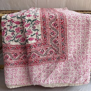 May include: A pink and white kantha quilt with a floral pattern. The quilt is made of cotton and is hand-stitched. It is a traditional Indian textile.