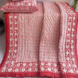 Peut inclure: Une couette en coton rouge et blanc avec un motif floral. La couette est pliée en deux et possède une bordure décorative. Il y a deux taies d'oreiller assorties avec le même motif.