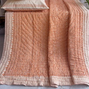 May include: A bed set comprising a quilt and two pillowcases. The bedding features an orange and white chevron pattern. The pillowcases and quilt have a decorative border. The set is made of a soft, comfortable material.