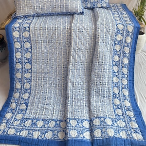 May include: A blue and white cotton quilt with a floral pattern. The quilt is made using a traditional block printing technique and features a geometric design. The quilt is ideal for adding a touch of bohemian style to any bedroom.