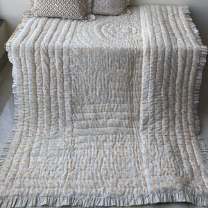 May include: A quilted throw blanket and two square throw pillows featuring a white, gray, and yellow geometric pattern. The blanket and pillows are finished with a ruffled fabric edge, creating a coordinated set with a soft, textured appearance.