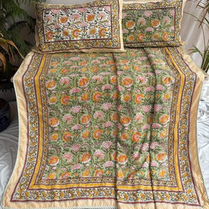 May include: A green floral bedspread with two matching pillowcases. The bedding features a repeating pattern of pink and orange flowers on a green background. The edges are trimmed with a yellow and brown border.