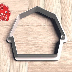 May include: A white plastic cookie cutter shaped like a barn with a simple design. The cutter is on a wood surface.