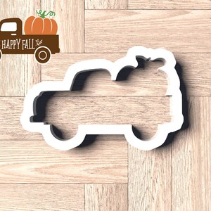 Pu&ograve; includere: Un tagliabiscotti bianco a forma di camion con una zucca nel cassone. Accanto, una grafica di camion marrone con una zucca, le parole "HAPPY FALL" e foglie decorative.