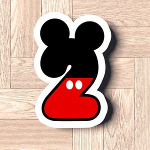 Puede incluir: Un número dos de Mickey Mouse de color rojo y negro. El número está rodeado de blanco y tiene dos círculos blancos en la parte roja.