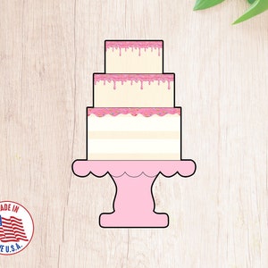 Puede incluir: Un pastel de tres pisos rosa y blanco con glaseado rosa y chispas en un soporte para pastel rosa.