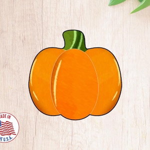 May include: A bright orange pumpkin cookie cutter with a green stem. The cookie cutter is on a woodgrain background.