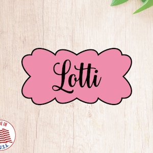 Könnte beinhalten: Rosaer Ausstecher in Wolkenform mit dem Namen "Lotti" in schwarzer Schrift.