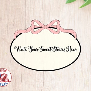 May include: A white oval frame with a pink bow on top. The frame has a black outline and the text "Write Your Sweet Stories Here" inside.