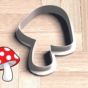 May include: White plastic mushroom cookie cutter on a wood background. A red and white mushroom illustration is also shown.