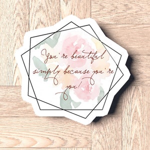 Peut inclure: Un autocollant blanc avec un cadre géométrique noir et un motif floral aquarelle. Le texte sur l'autocollant est "You're beautiful simply because you're you!"