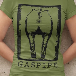 May include: Olive green t-shirt with a black graphic of a horse's rear end inside a black rectangular frame. The word "GASPIPE" is printed in black below the graphic. The model is wearing black denim shorts.