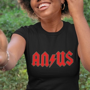 May include: Black t-shirt with the red text "AQ/US" and a lightning bolt graphic. The text has a silver outline. The person is smiling and wearing gold hoop earrings.