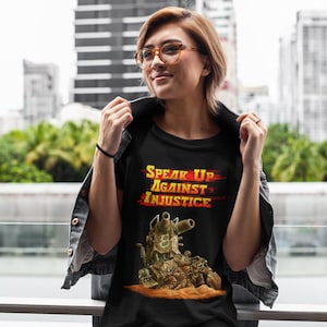 May include: Black t-shirt featuring a graphic of a tank and the text "Speak Up Against Injustice" in yellow and red.