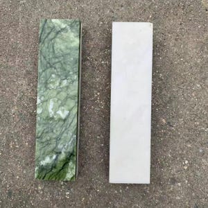 Puede incluir: Dos losas de piedra rectangulares. Una es de un verde vibrante con vetas oscuras, la otra es blanca sólida. Las losas están una al lado de la otra, mostrando el contraste de color y textura. La losa verde tiene un aspecto veteado.