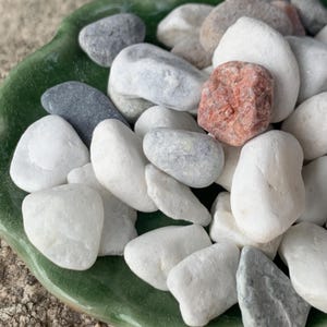 May include: A selection of smooth, polished stones in shades of white, grey, and reddish-brown. The stones are presented on a green, leaf-shaped dish, offering a natural and decorative aesthetic. Suitable for home decor or craft applications.