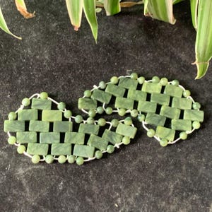 May include: Two green jade stone face rollers connected by a white string. The rollers are made of small, rectangular pieces of jade, creating a grid pattern.