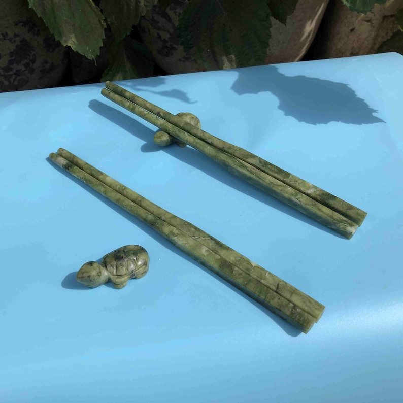 Op de afbeelding: Een set groene stenen eetstokjes met een bijpassende schildpadvormige eetstokjeshouder. De eetstokjes zijn lichtgroen van kleur met donkerdere groene adering. De schildpad eetstokjeshouder is klein en gedetailleerd.