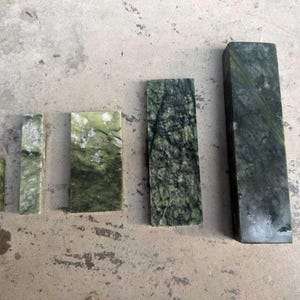 May include: Five rectangular jade stones of varying sizes are arranged on a concrete surface. The stones display a range of green hues with natural veining patterns. The largest stone is approximately 20 cm tall.