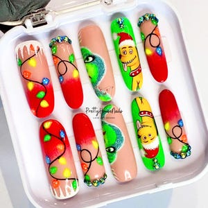 May include: Set of ten false nails with Christmas-themed designs. The nails feature a Grinch, a dog wearing a Santa hat, and red and white Christmas lights. The nails are in a white box with the text "Pretty House Nails Love Life Design".