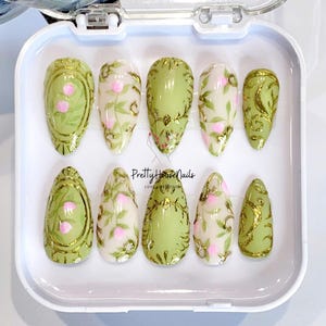 Unghie finte a mandorla verde menta dipinte a mano con motivi floreali, dettagli scolpiti in oro, nail art alla moda per un look elegante, unghie uniche.
