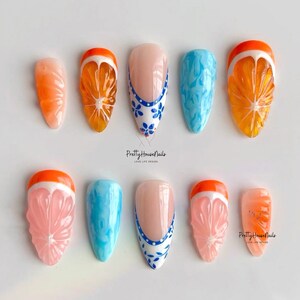 May include: Set of ten false nails with various designs.  Some nails feature a blue and white floral design, while others have a 3D orange slice design.  The text "PrettyHouseNails Love Life Design" appears twice in the image.