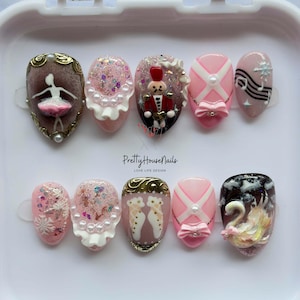May include: A set of ten artificial nails with various designs. The nails feature ballet-themed art, including a ballerina, a nutcracker, and a swan. Other nails have pink and white patterns, glitter, and musical notes. The text "Pretty House Nails" is visible.
