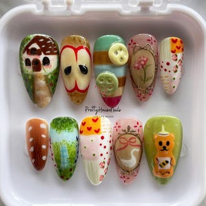 Juego de uñas con diseño de naturaleza caprichosa con oso, manzana, botones y flores. Uñas postizas artesanales de estilo cottagecore, uñas de fiesta y uñas kawaii.
